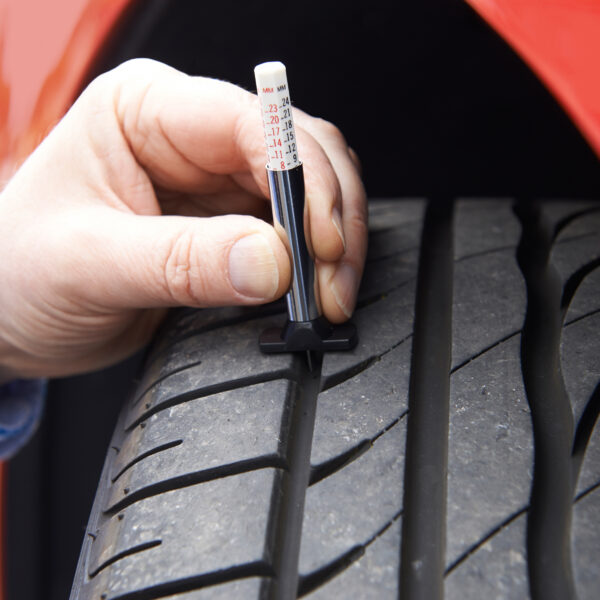 A red car with a black tire in main frame. a man's hand in the frame checking the tire pressure with a tool.
