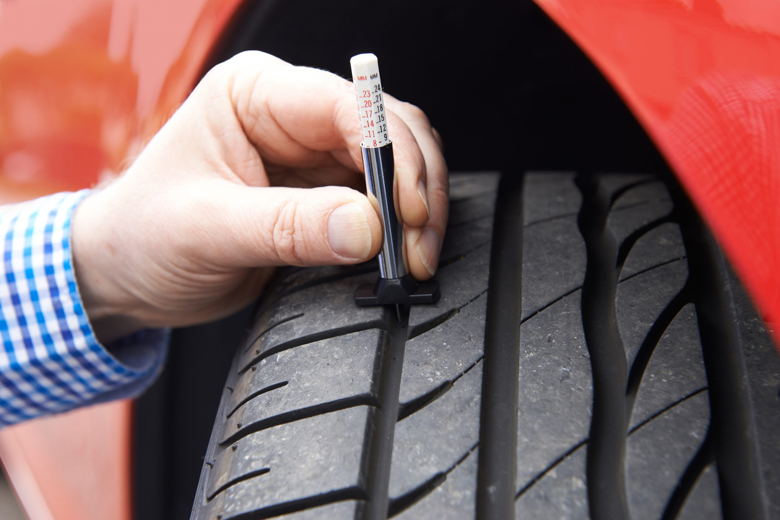 A red car with a black tire in main frame. a man's hand in the frame checking the tire pressure with a tool.